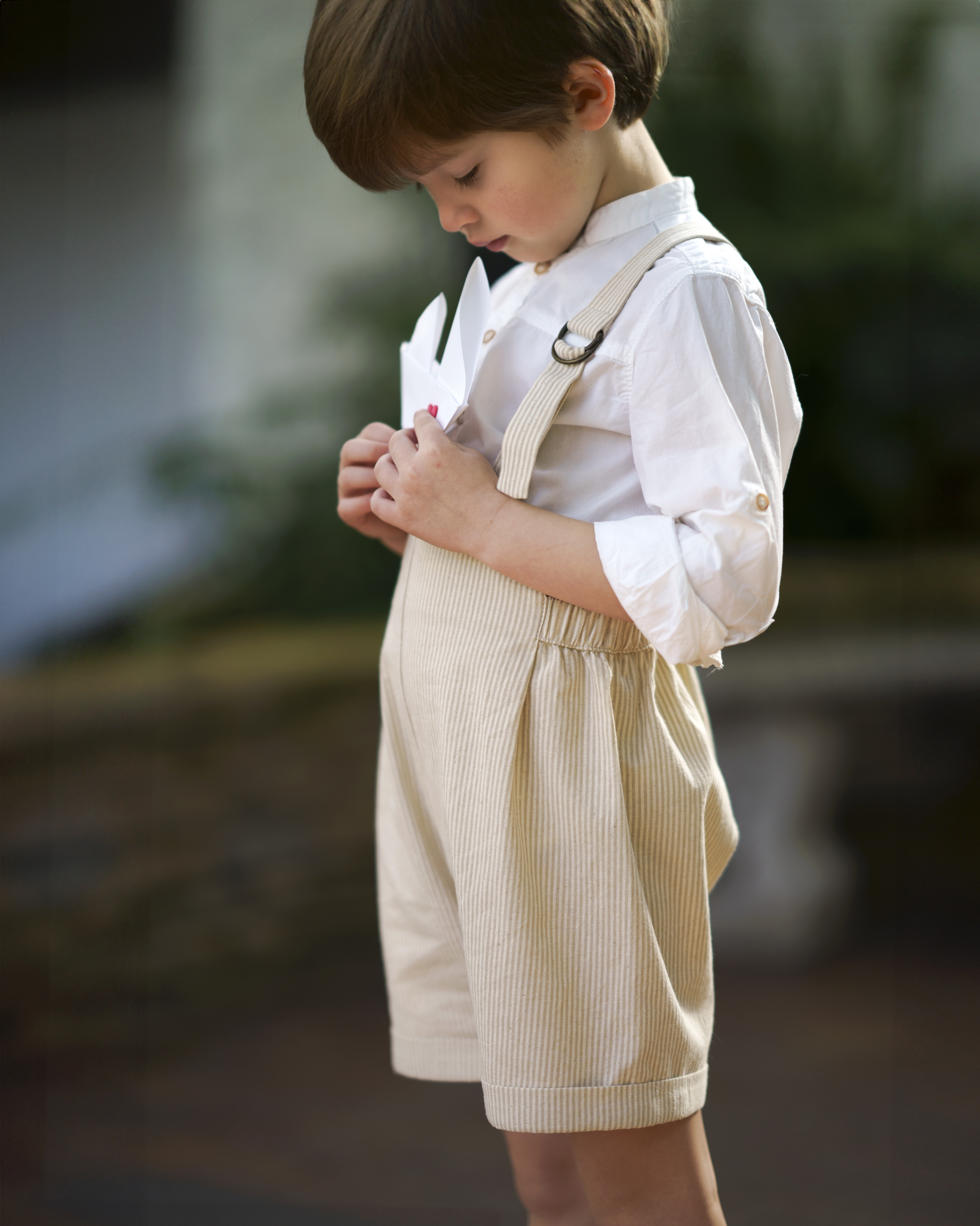 Little 5-year-old model wearing the Grow-With-Me Romper - Beige Stripes, showcasing the fully adjustable straps for a perfect fit, the classic timeless beige stripes pattern, and the comfortable, soft fabric ideal for all-day wear, embodying playful elegance in sustainable children's fashion.