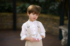 Little boy showcasing details of the Grow-With-Me Romper - Beige Stripes, highlighting the fully adjustable straps for a customizable fit, the classic timeless beige stripes pattern, and the soft, breathable fabric that ensures comfort throughout the day, representing stylish versatility in sustainable children's attire.