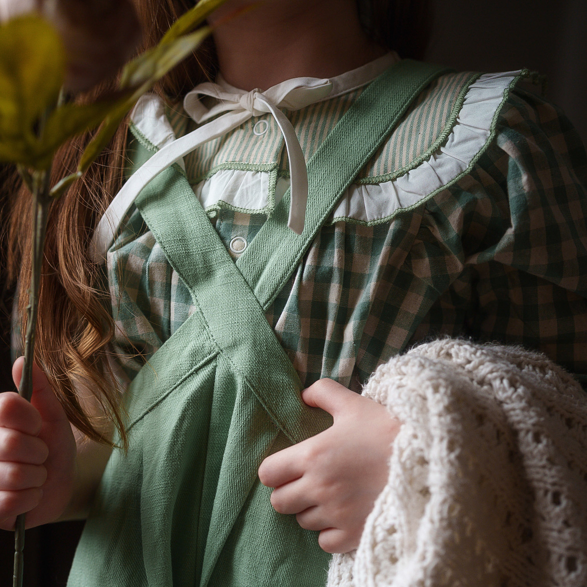 Person wearing a green apron with a checkered shirt underneath, holding a white lace garment.