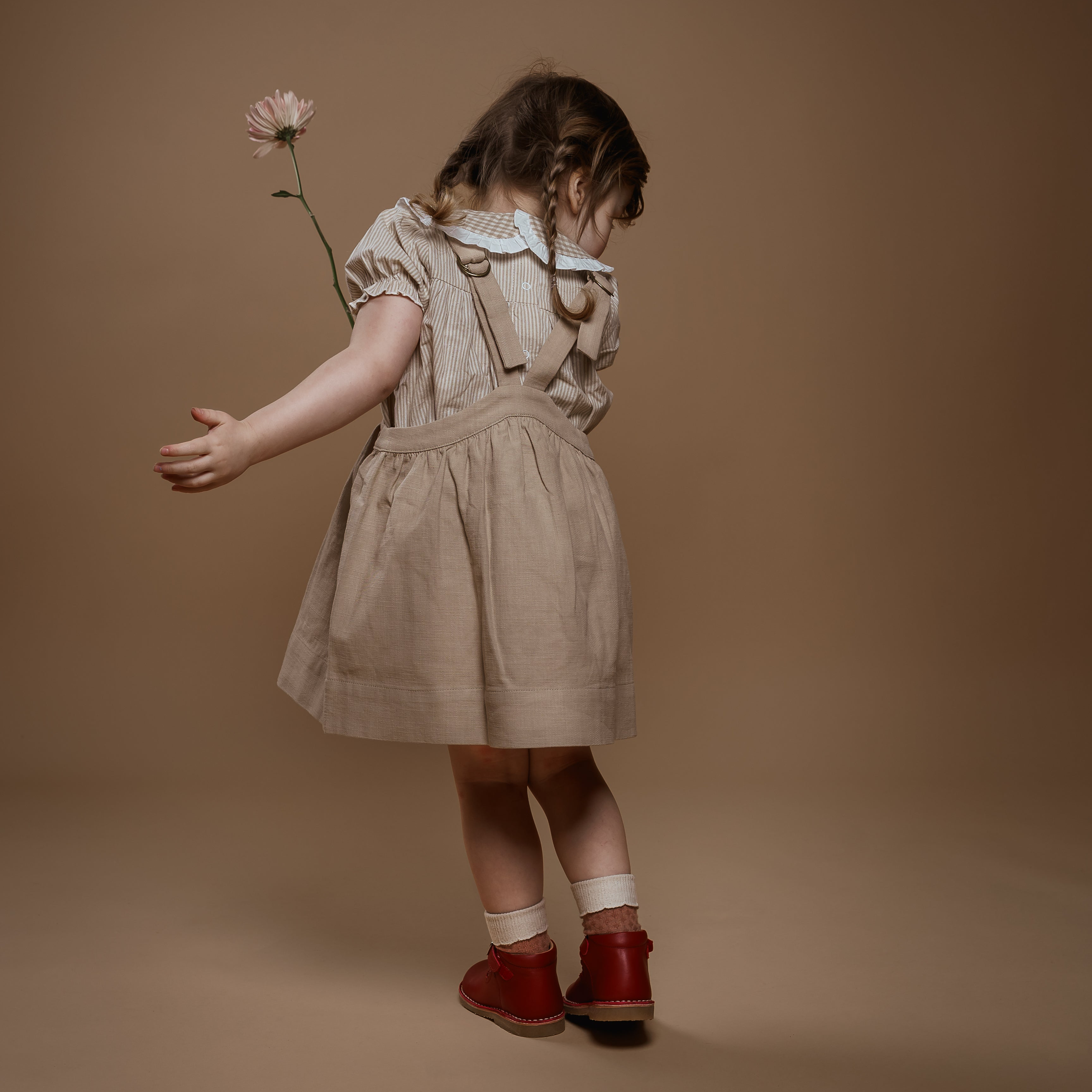 Young girl in a beige dress holding a flower against a brown background