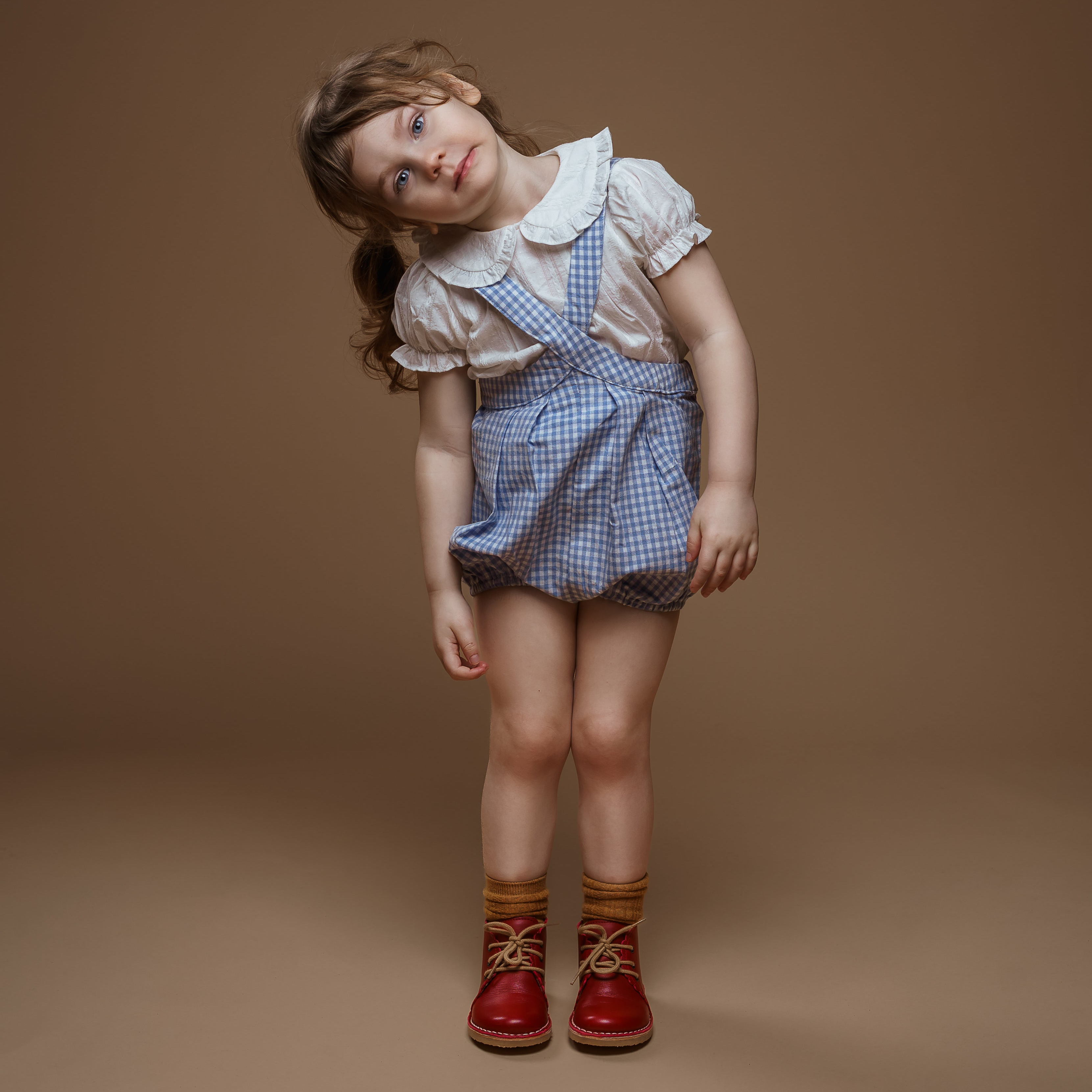 Young girl in a checkered dress and red boots on a brown background
