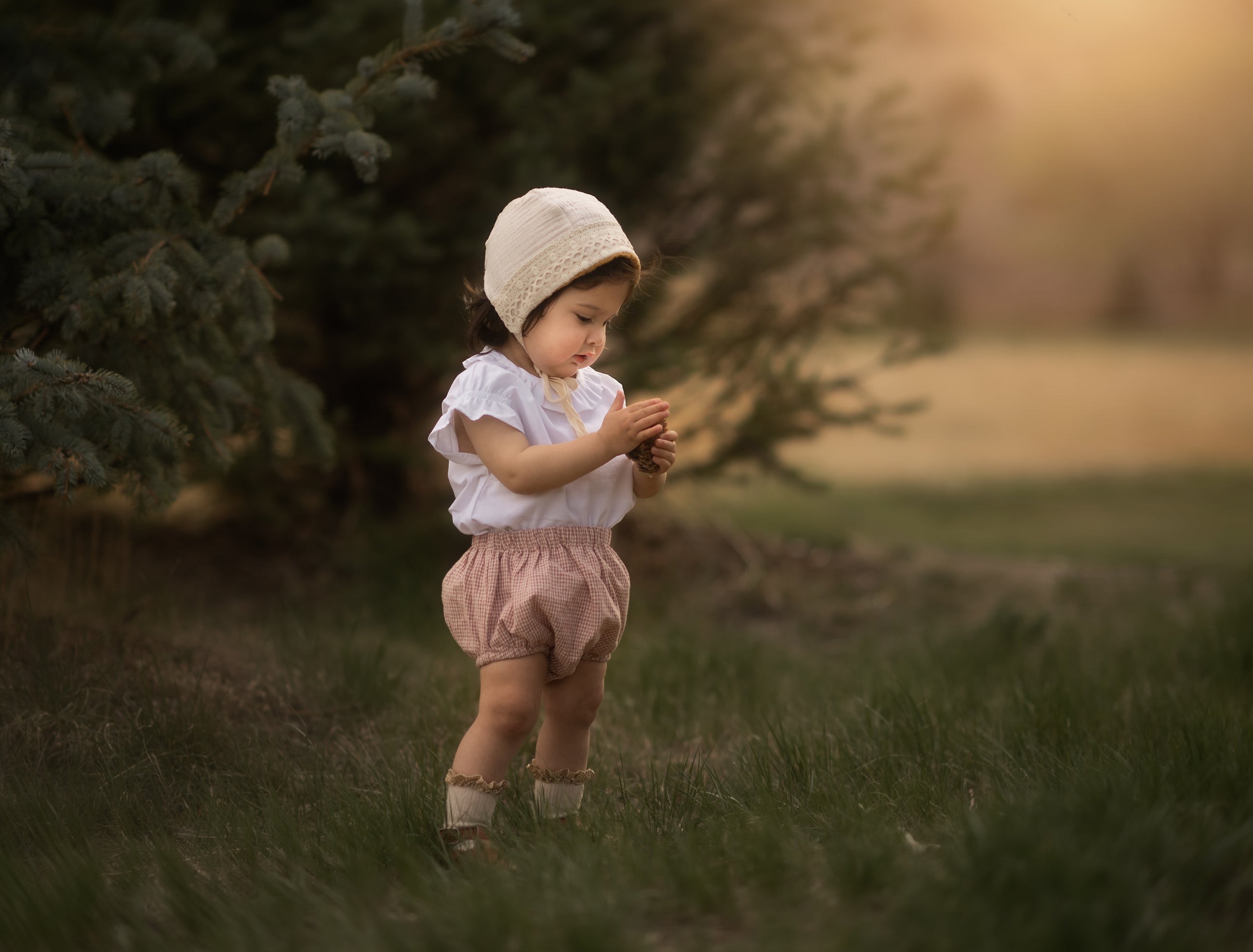 Baby in a bonnet and bloomers in a blurred field playing with her hands