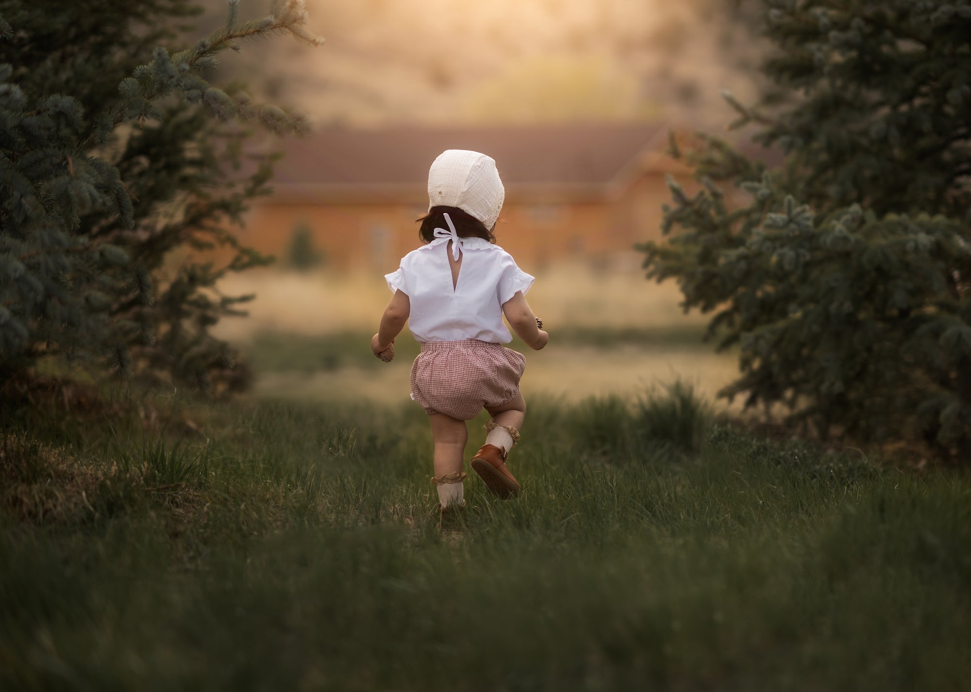 Baby in a bonnet and bloomers in a blurred field walking away
