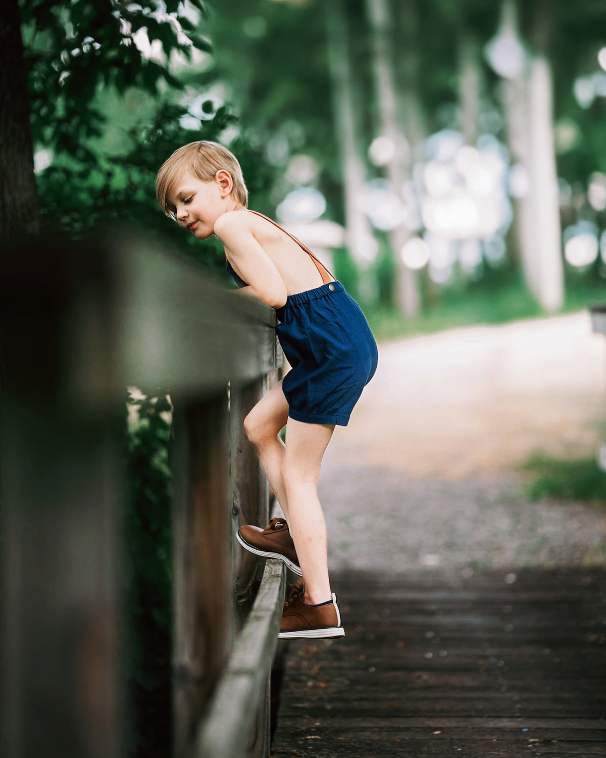 Boy in navy overalls climbing over a fence