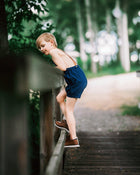 Boy in navy overalls climbing over a fence