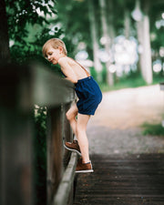 Boy in navy overalls climbing over a fence