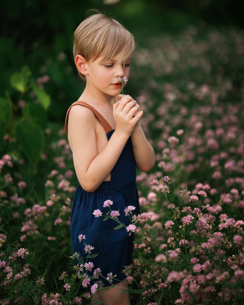 Boy in navy overalls smelling flowers in a field of flowers