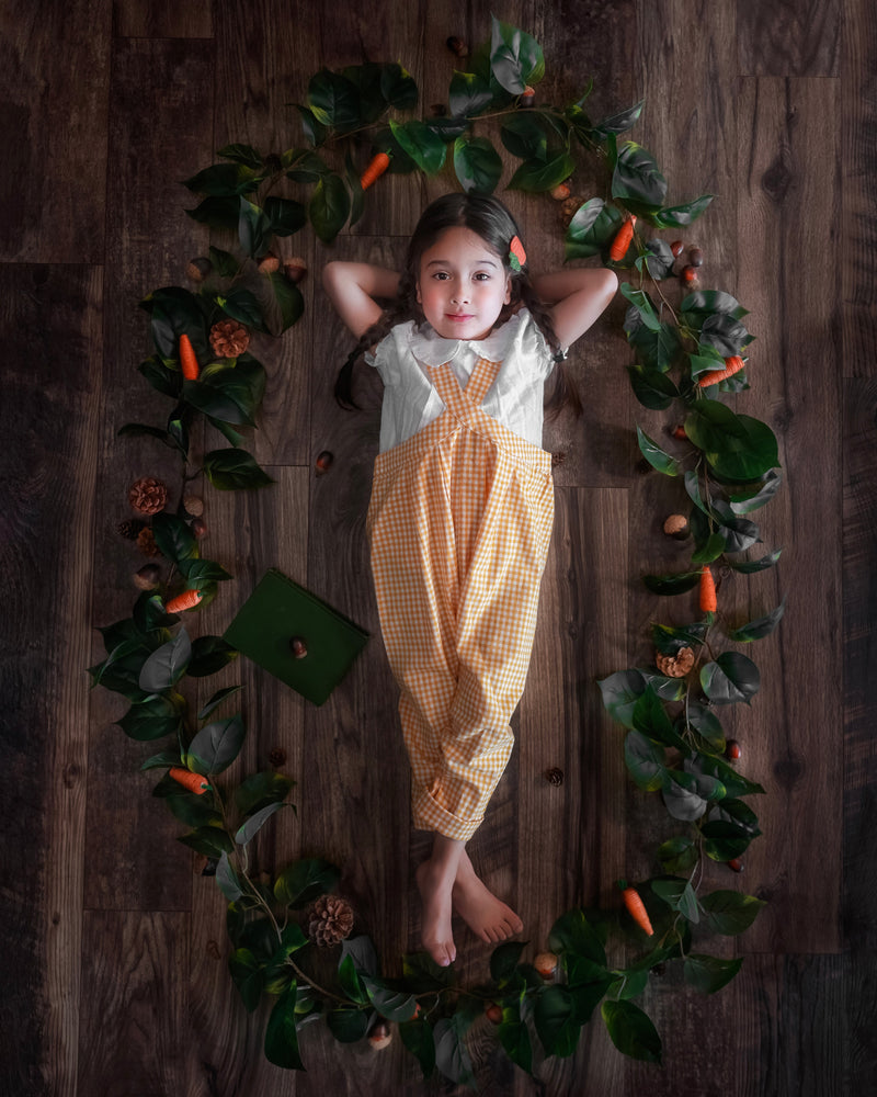 Child in a checkered outfit lying on a wooden floor with decorative elements