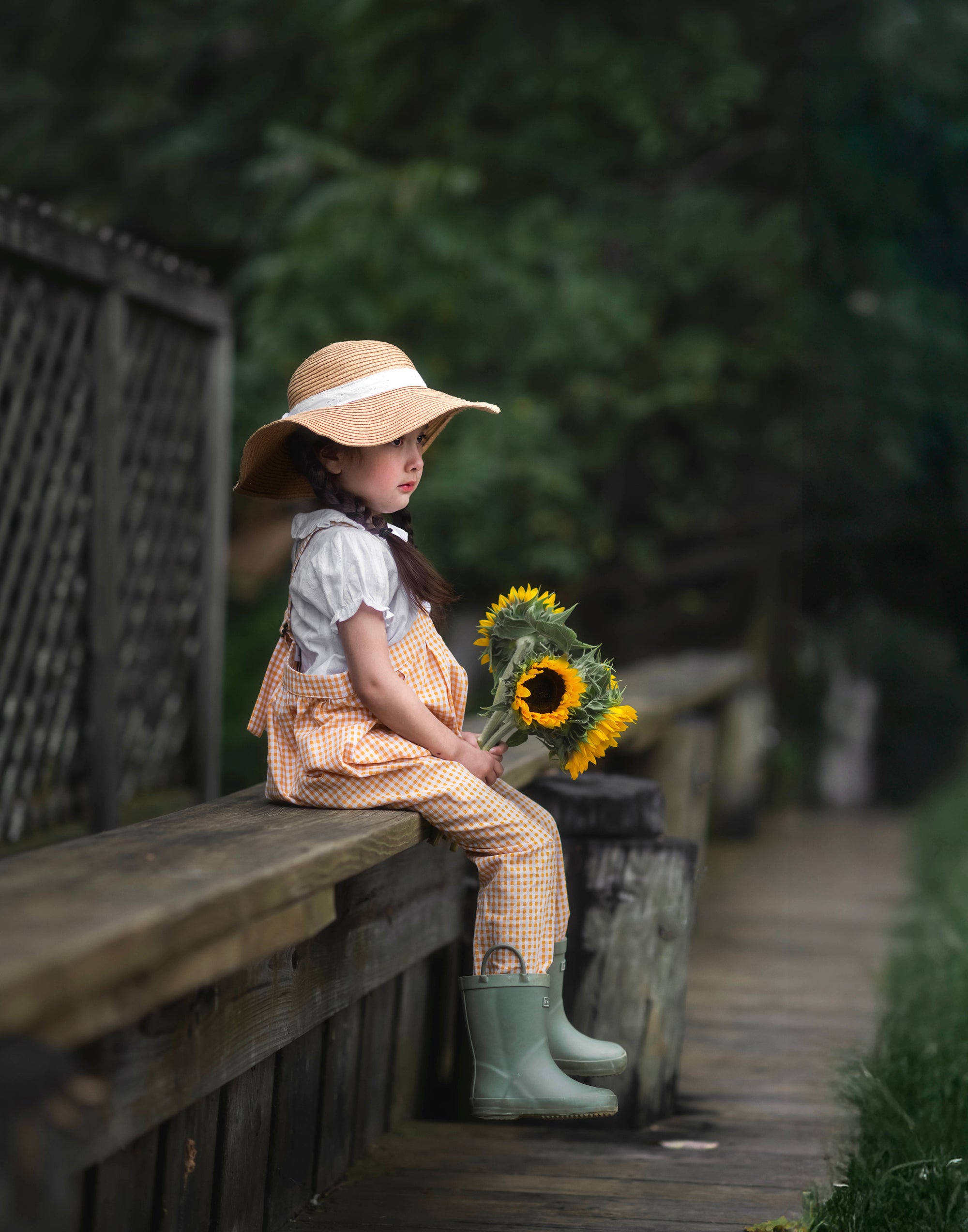 Girl sitting on a wooden bench holding sunflowers in a natural setting