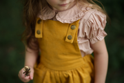Close-up of the bib detail on the Mustard Pinafore, featuring a generous pocket designed for little treasures, showcasing the quality craftsmanship of our handmade children’s wear.