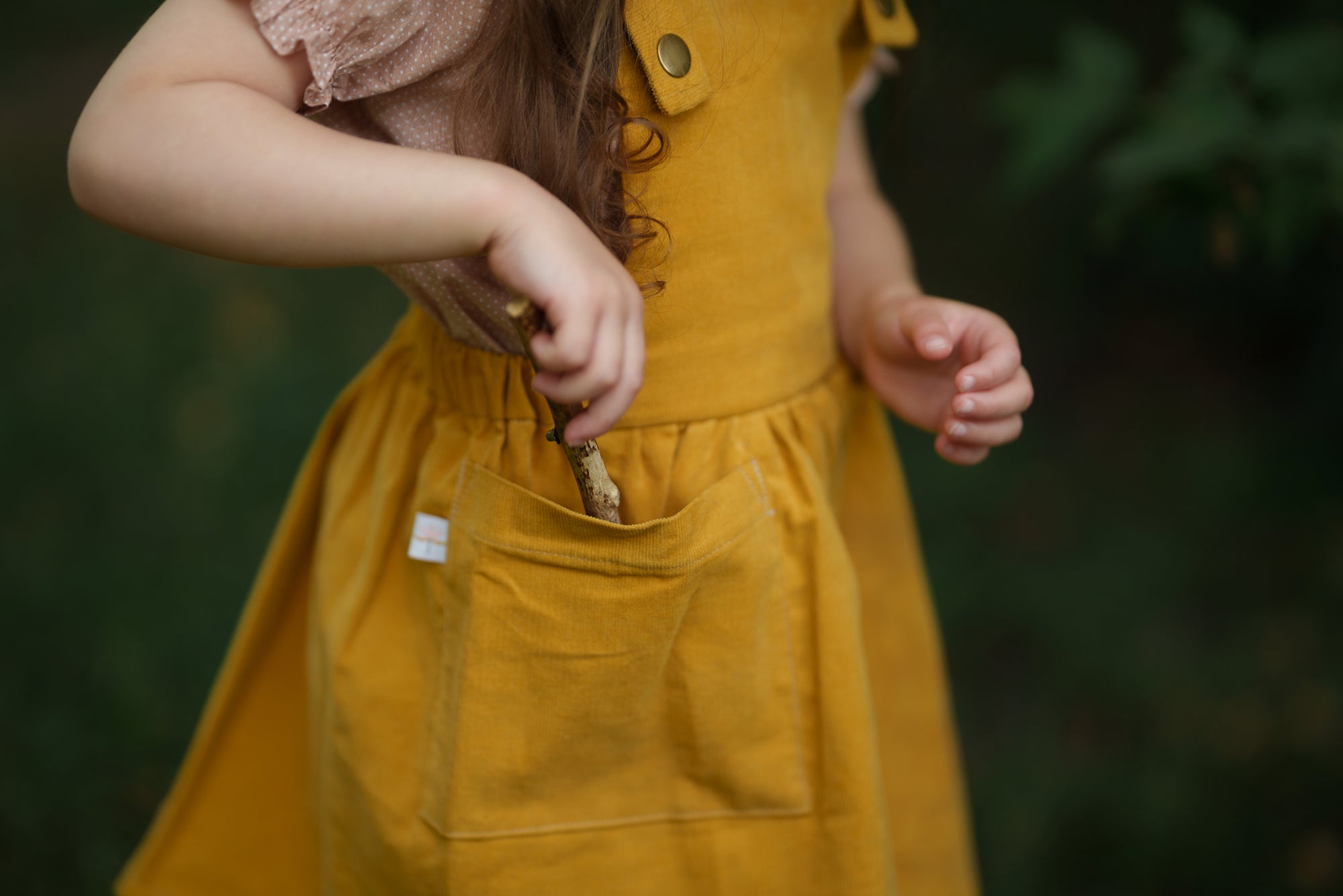 Detail view of the large patch pocket on the Mustard Pinafore worn by a model, emphasizing its practical design and the use of repurposed materials in our sustainable collection.