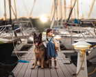 Child and German Shepherd dog on a dock with boats in the background
