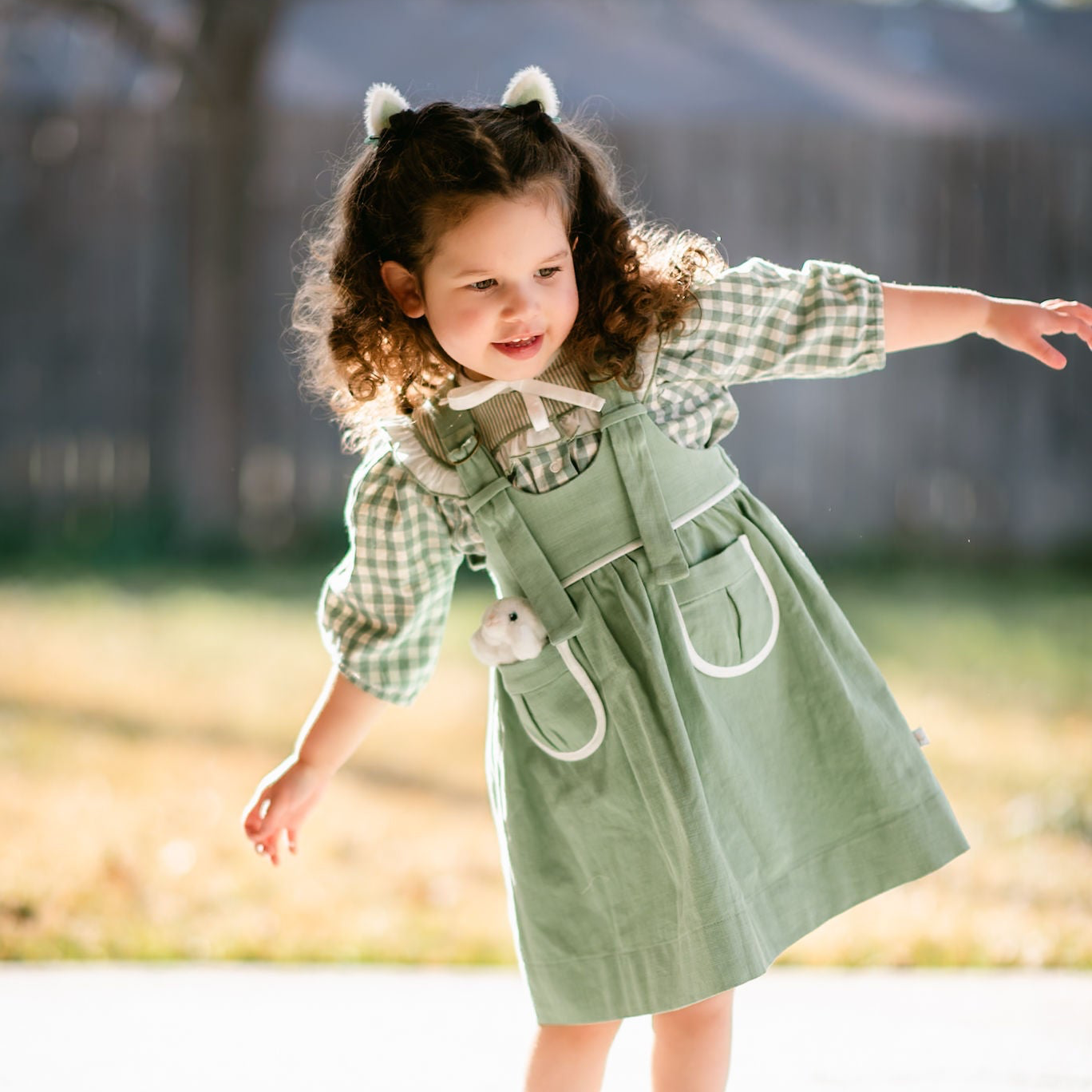 Child in a green dress with white apron and checkered shirt outdoors