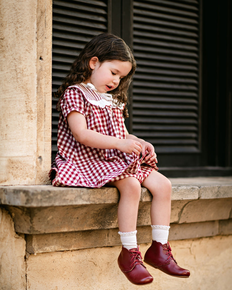 Young girl in a red checkered dress sitting on a stone ledge.