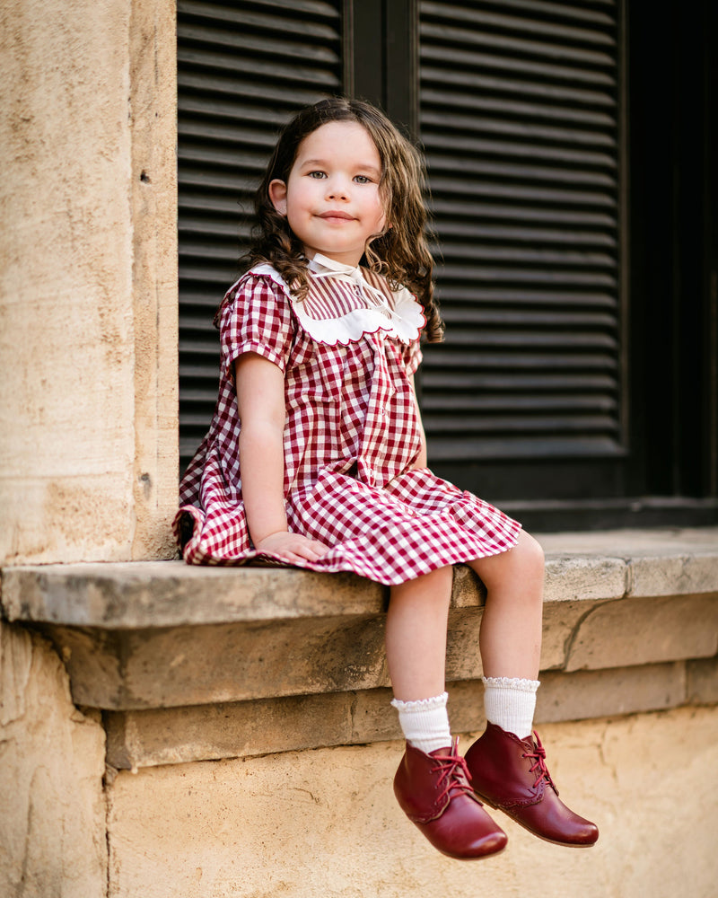 Young girl in a red checkered dress sitting on a stone ledge.