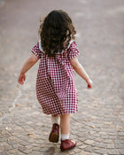 Child in a red and white checkered dress walking on a cobblestone street.