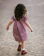 Child in a red and white checkered dress walking on a cobblestone street.