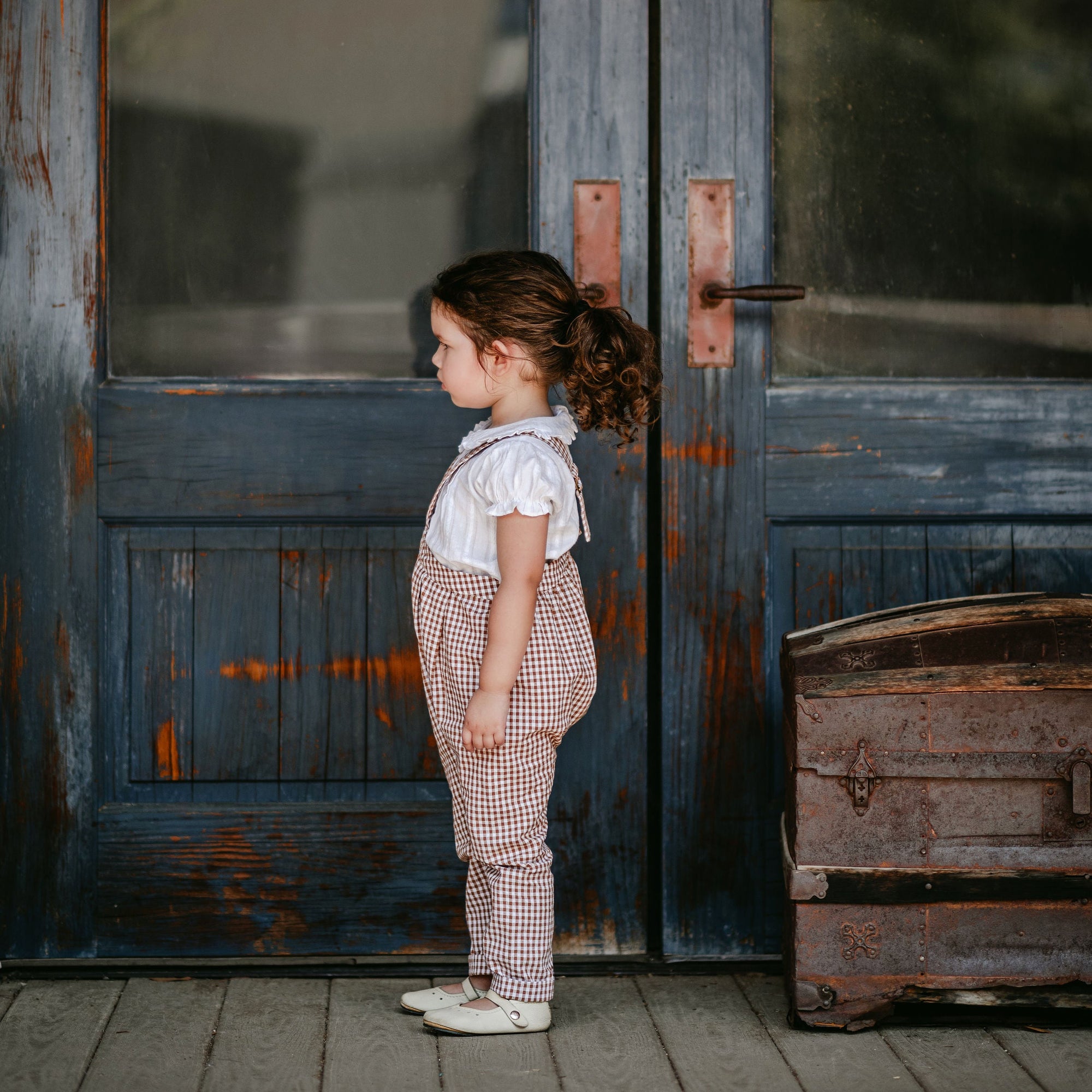 Child standing in front of a rustic wooden door with 'Daily News' written on it.