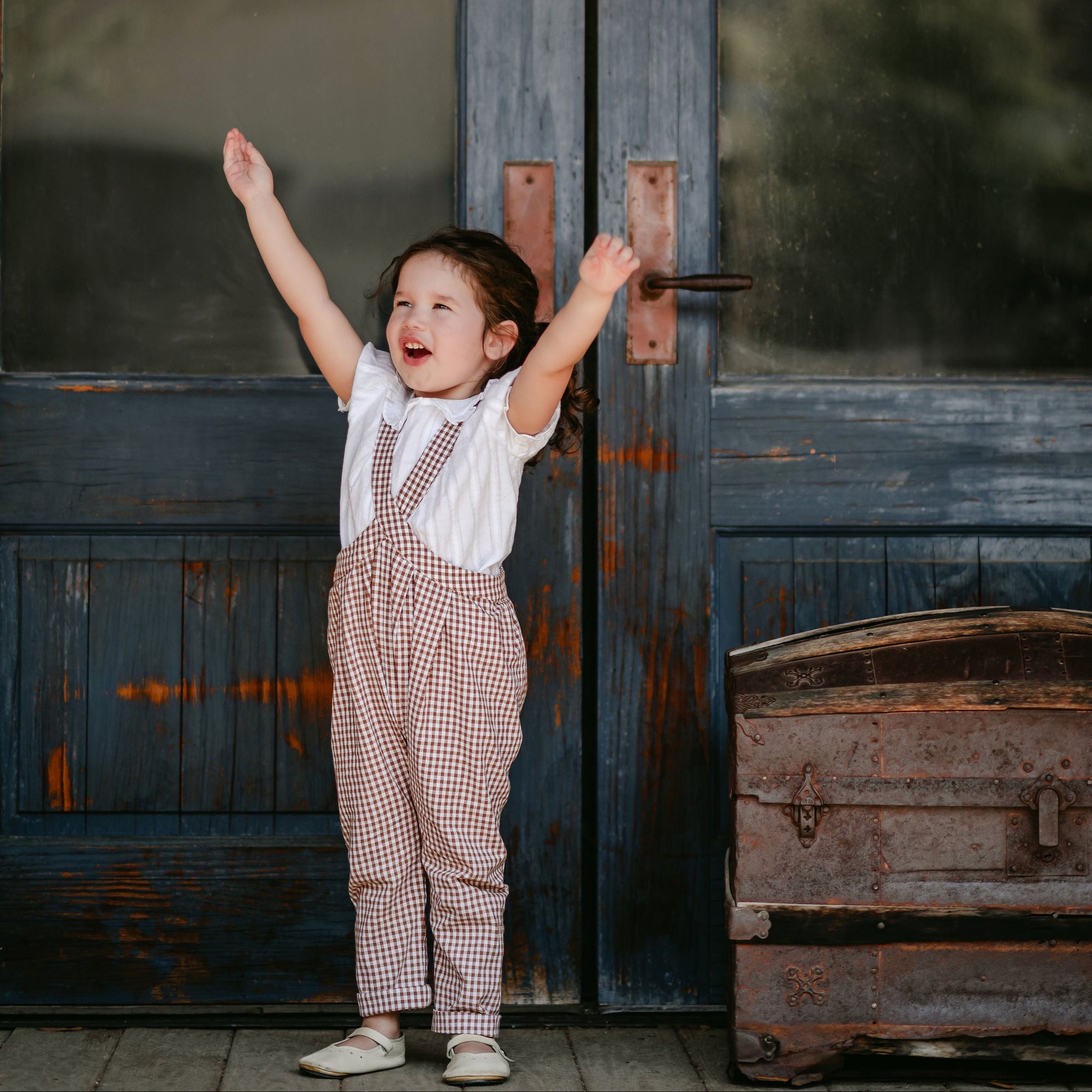 Child with arms raised in front of a large door with 'Daily News' printed on it.