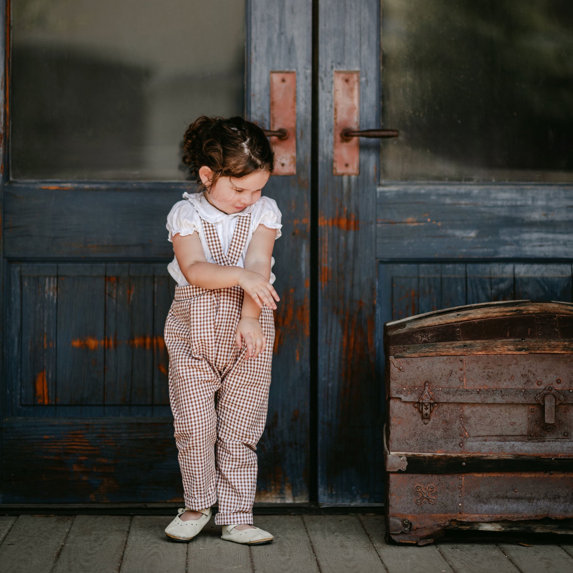 Child standing in front of a large wooden door with 'Daily News' signage.