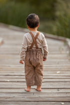 Child wearing brown suspenders and pants on a wooden pathway