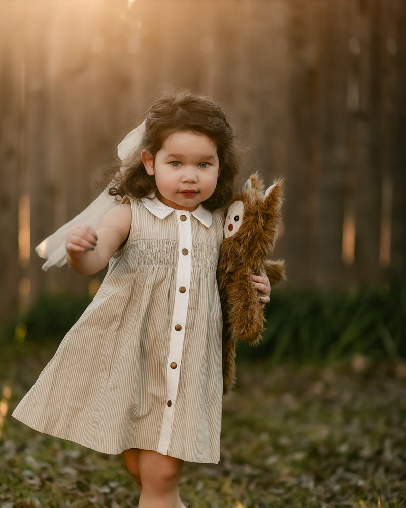 girl in a beige striped dress walking with toy monster