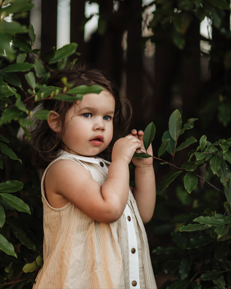 girl in a beige striped dress holding plants