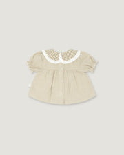 A baby girl's short-sleeve blouse in beige and white vertical stripes, featuring a white ruffled Peter Pan collar with a beige and white gingham pattern, set against a solid light gray background.