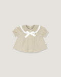 A baby girl's short-sleeve top in beige and white vertical stripes, featuring a white gingham Peter Pan collar, a white bow at the neckline, and a small white side tag, shown on a solid light gray background.