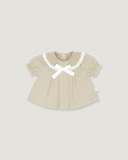 A baby girl's short-sleeve top in beige and white vertical stripes, featuring a white gingham Peter Pan collar, a white bow at the neckline, and a small white side tag, shown on a solid light gray background.