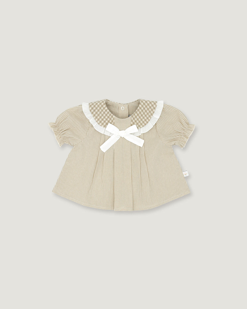 A baby girl's short-sleeve top in beige and white vertical stripes, featuring a white gingham Peter Pan collar, a white bow at the neckline, and a small white side tag, shown on a solid light gray background.