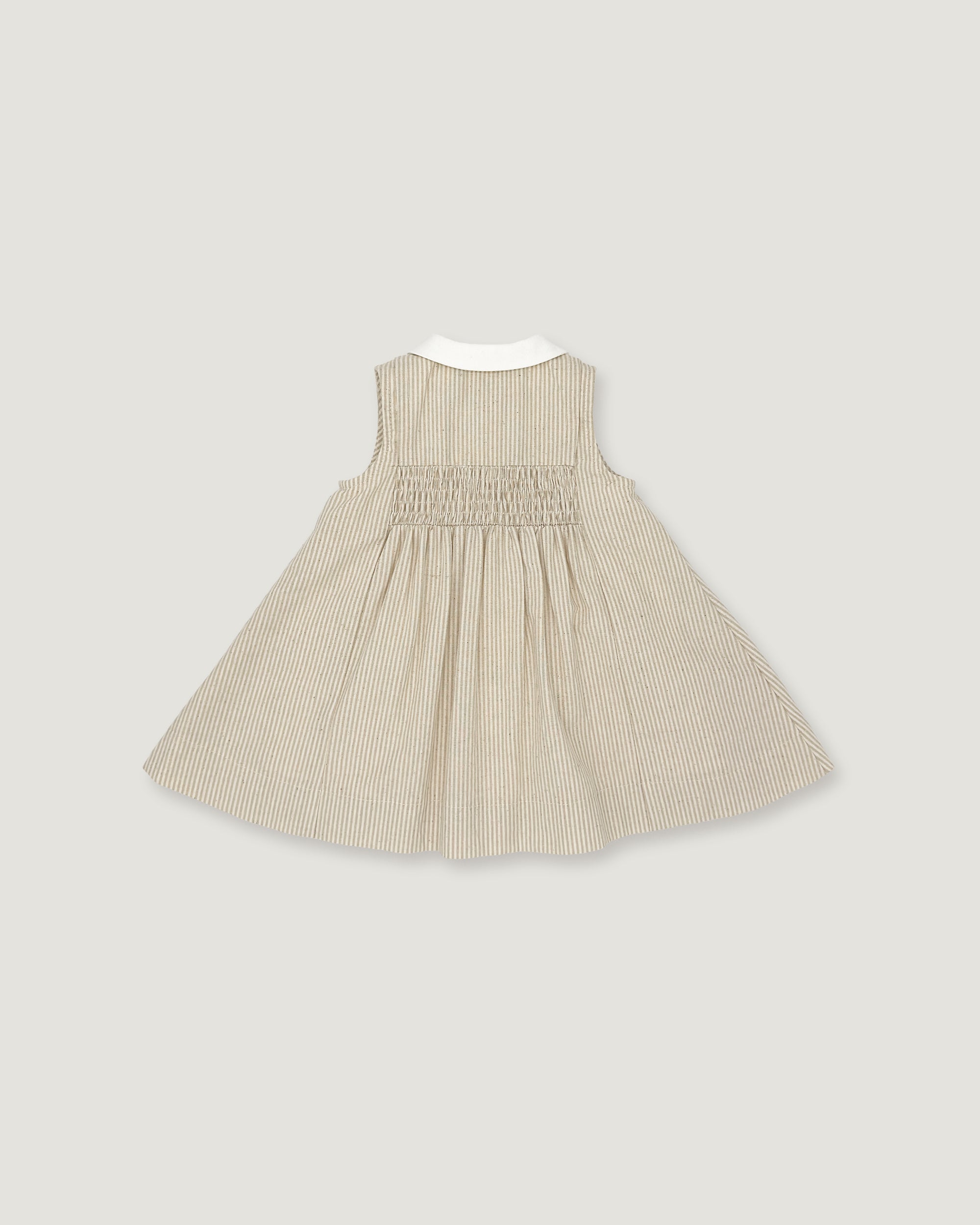 A sleeveless baby dress in beige and white vertical pinstripes, featuring a smocked bodice and a contrasting white collar, shown flat against a light gray background.