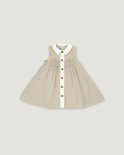 A sleeveless baby dress in beige and white vertical pinstripes, featuring a white Peter Pan collar, a smocked bodice, and a front button closure with gold-tone buttons, shown flat on a light gray background.