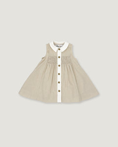 A sleeveless baby dress in beige and white vertical pinstripes, featuring a white Peter Pan collar, a smocked bodice, and a front button closure with gold-tone buttons, shown flat on a light gray background.