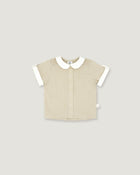 A short-sleeve baby shirt in beige ribbed fabric with a white Peter Pan collar, white sleeve cuffs, and a subtle checkered pattern on the shoulders, shown on a solid light gray background.