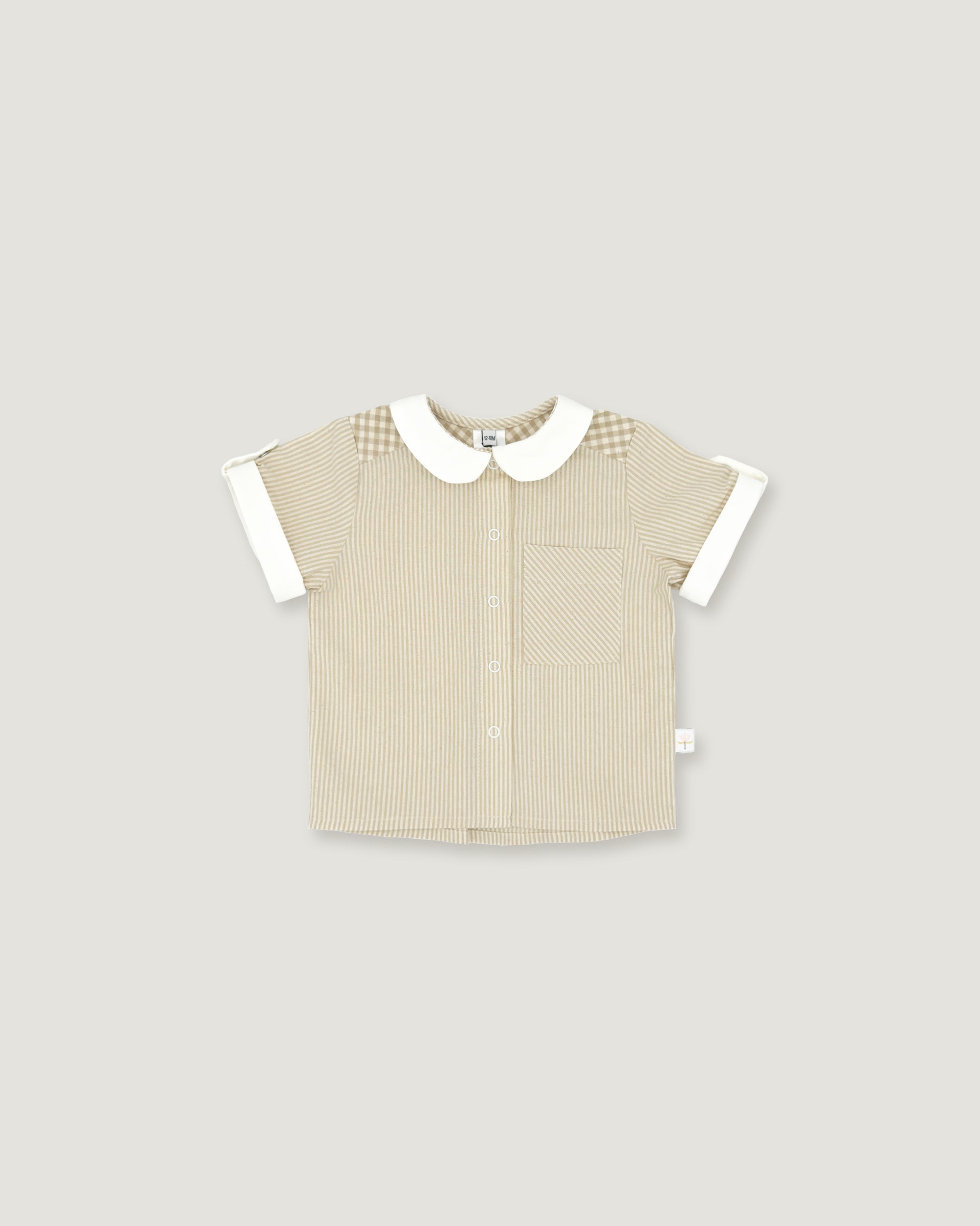 A short-sleeve baby shirt in beige ribbed fabric with a white Peter Pan collar, white sleeve cuffs, and a subtle checkered pattern on the shoulders, shown on a solid light gray background.