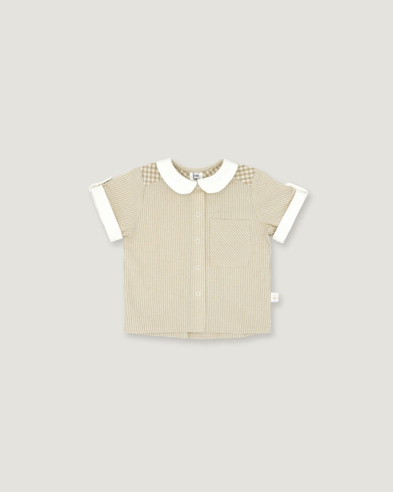 A short-sleeve baby shirt in beige ribbed fabric with a white Peter Pan collar, white sleeve cuffs, and a subtle checkered pattern on the shoulders, shown on a solid light gray background.