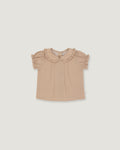 A toddler girl's short-sleeve blouse in a light beige or dusty tan color, featuring a ruffled Peter Pan collar and ruffled sleeves, laid flat against a solid light gray background.