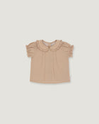 A toddler girl's short-sleeve blouse in a light beige or dusty tan color, featuring a ruffled Peter Pan collar and ruffled sleeves, laid flat against a solid light gray background.