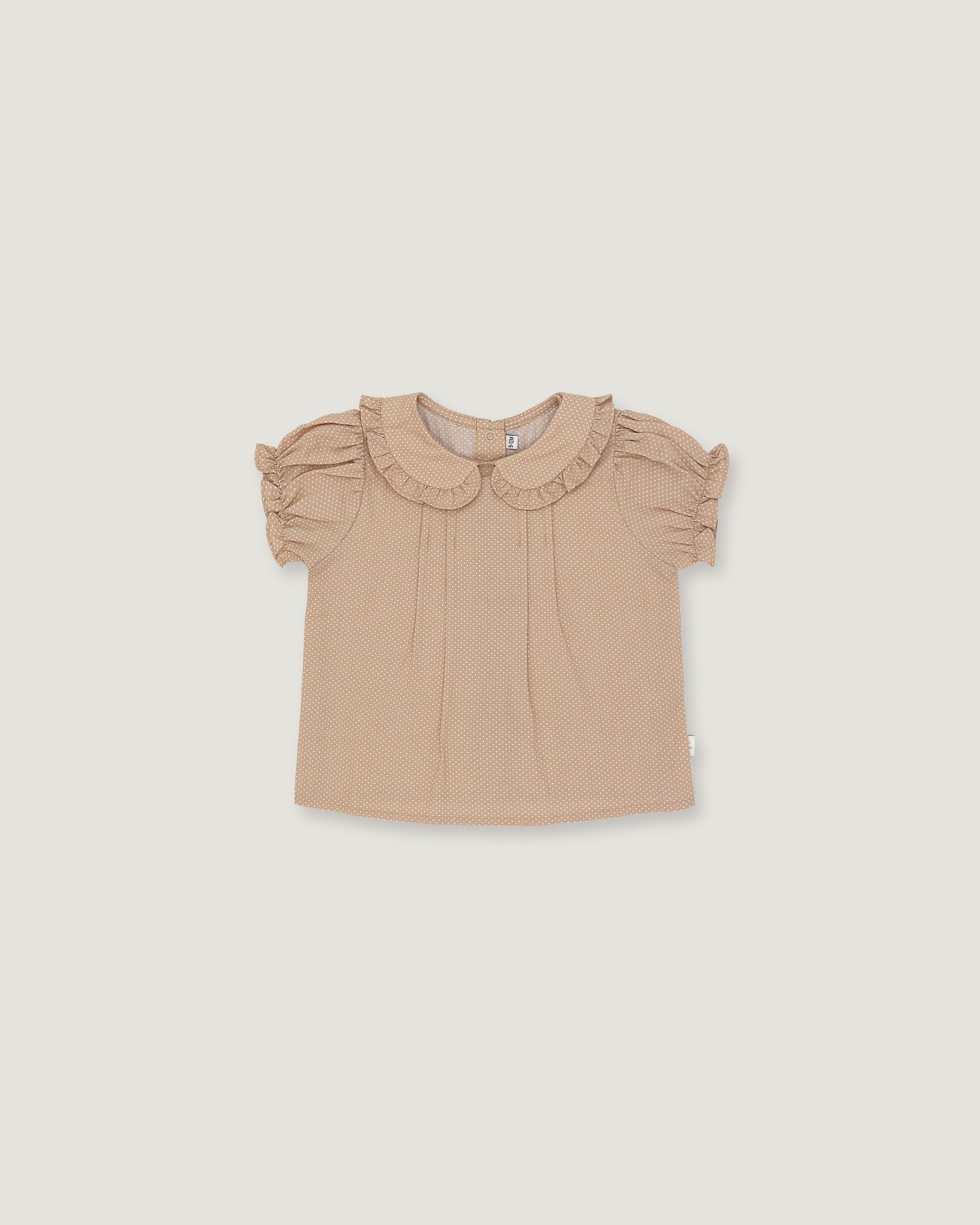 A toddler girl's short-sleeve blouse in a light beige or dusty tan color, featuring a ruffled Peter Pan collar and ruffled sleeves, laid flat against a solid light gray background.