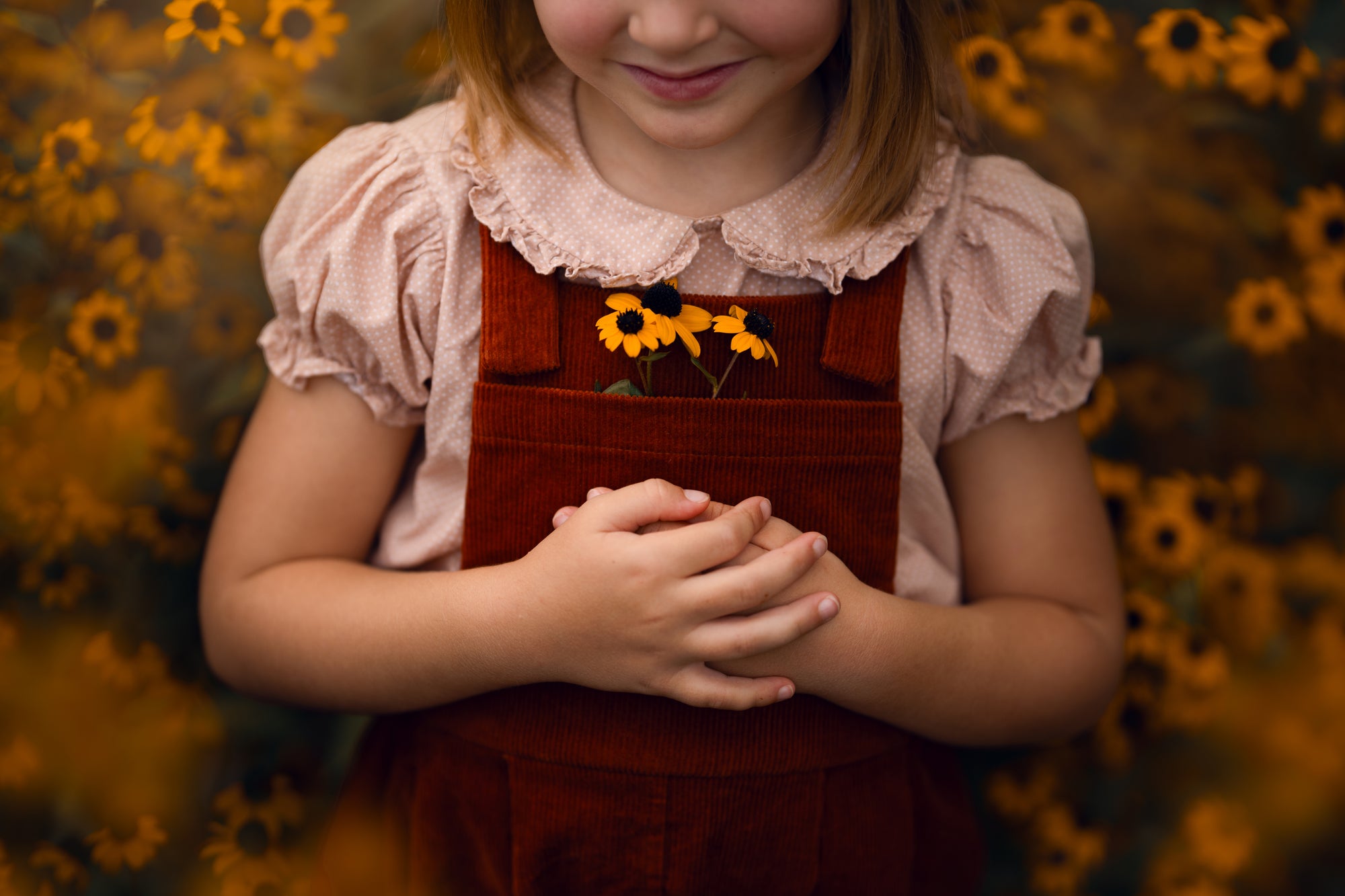 Child wearing a red apron with yellow flowers, standing against a blurred natural background.