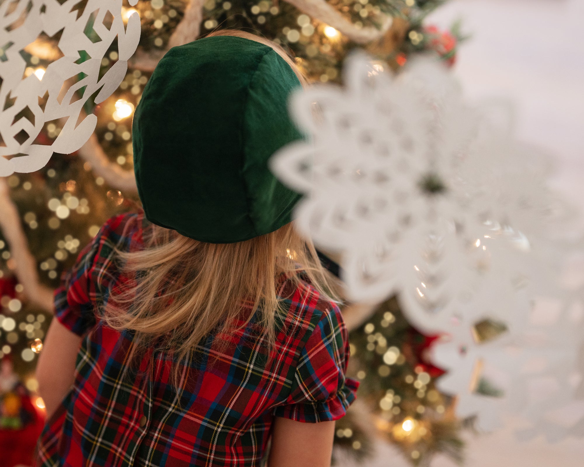 Girl in a green bonnet surrounded by Xmas decorations seen from the back