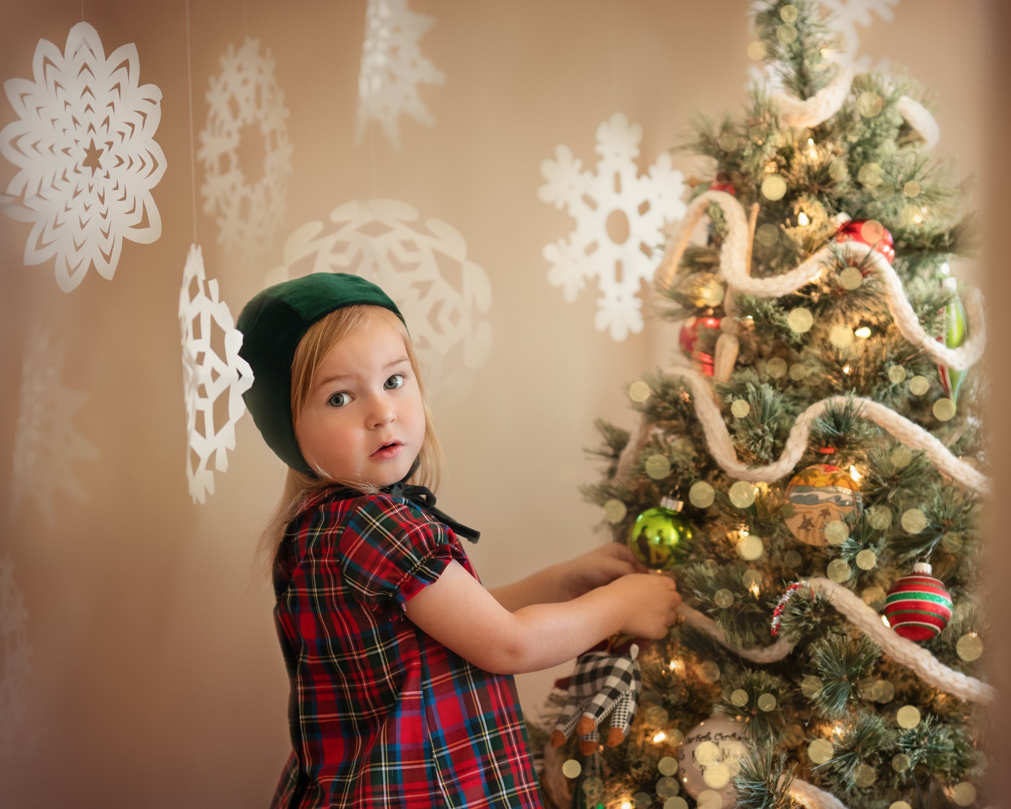 Girl in green bonnet and plaid blouse decorating a Xmas tree