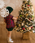 Girl in green bonnet and plaid blouse decorating a Xmas tree