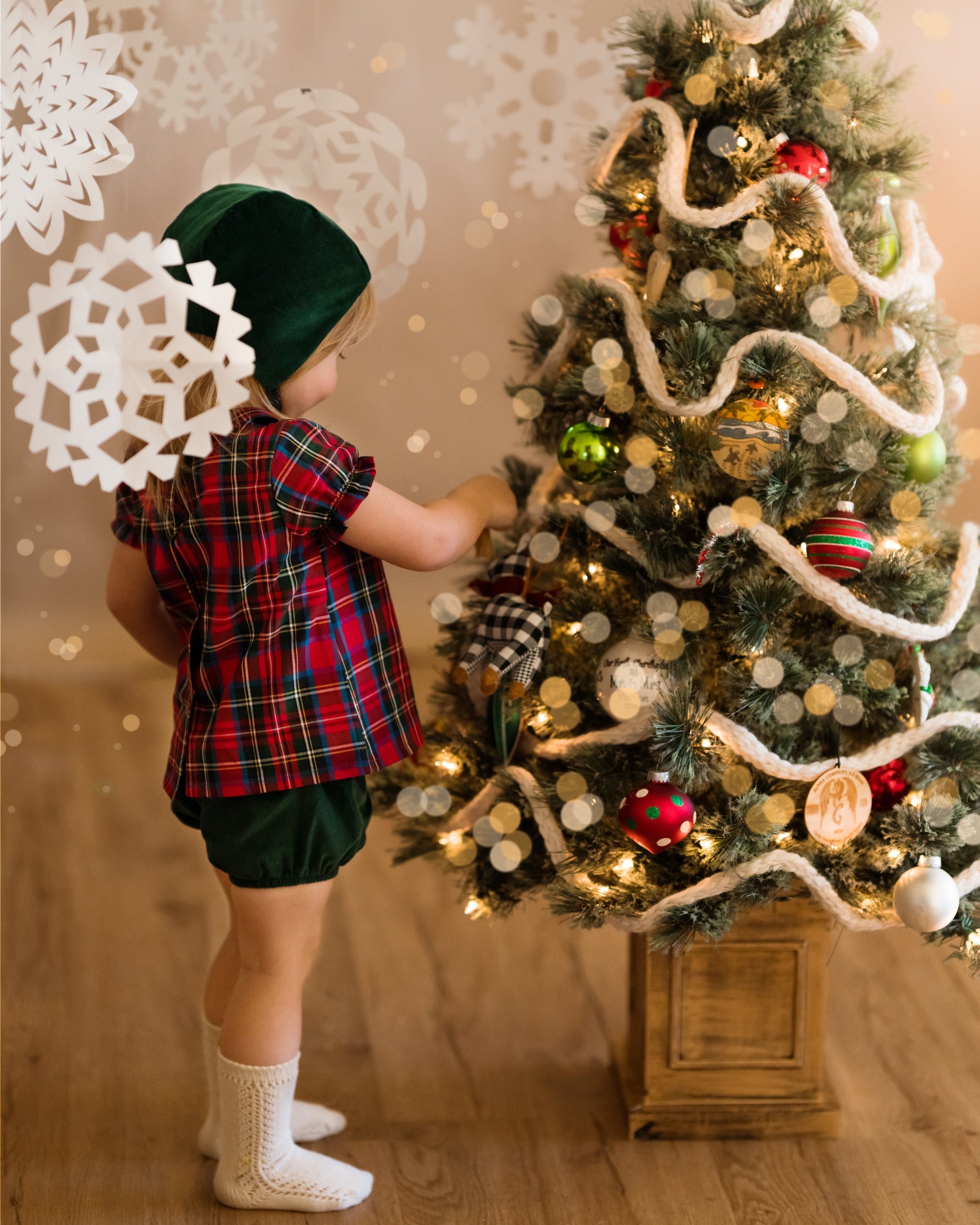Girl in green bonnet and plaid blouse decorating a Xmas tree