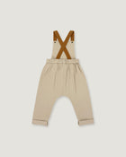 A pair of beige toddler pants with brown suspenders, laid flat against a light gray background.