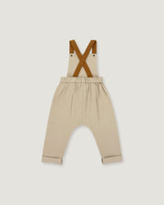 A pair of beige toddler pants with brown suspenders, laid flat against a light gray background.