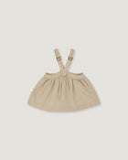 A light beige baby dress with adjustable shoulder straps and a gathered skirt, shown flat on a light gray background.