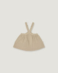 A light beige baby dress with shoulder straps, laid flat against a solid light gray background.