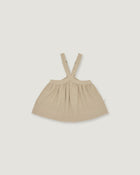 A light beige baby dress with shoulder straps, laid flat against a solid light gray background.